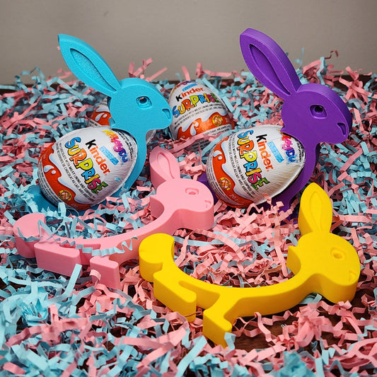 An assortment of 3d printed bunnies sitting in coloured paper holding kinder surprise eggs