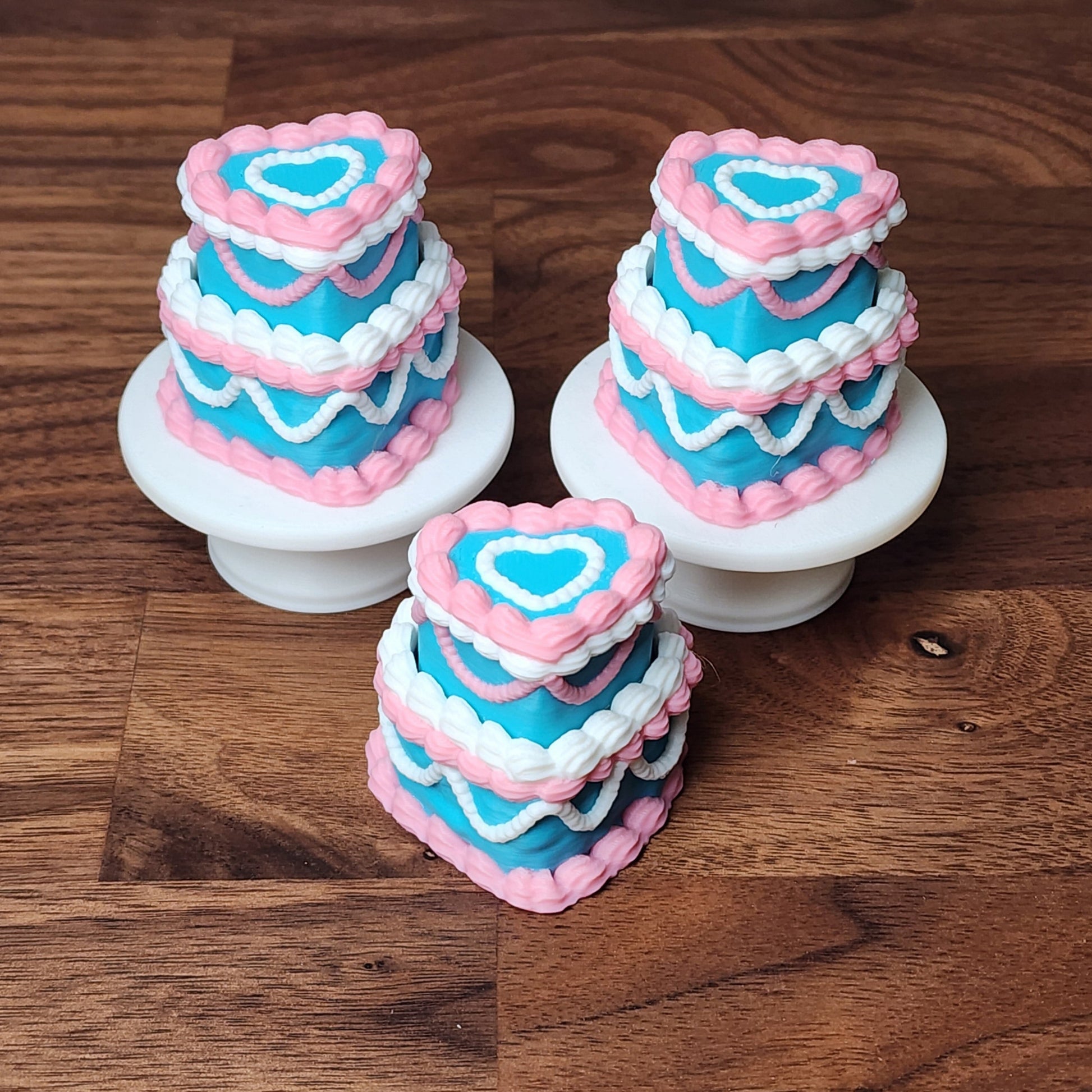 Three miniature 3D printed heart-shaped cake fidget clickers with pink, blue and white frosting 