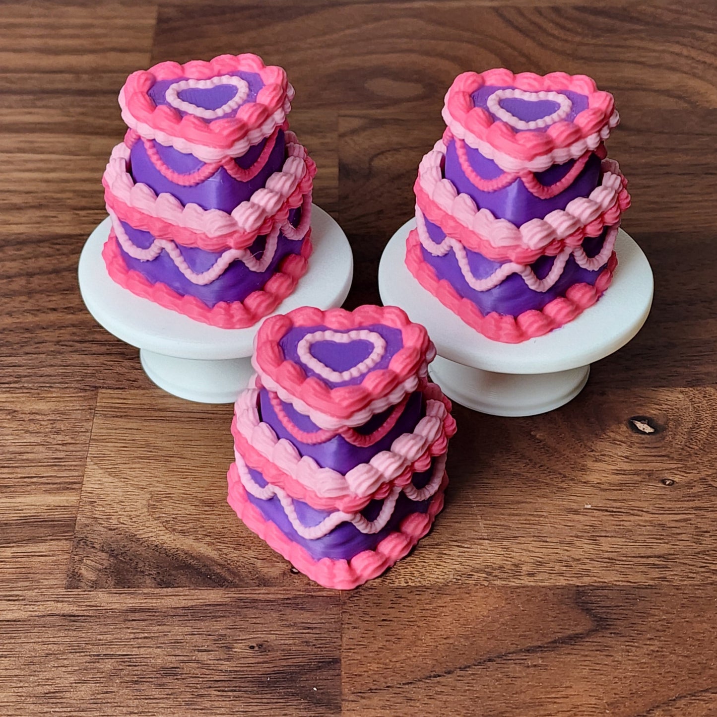 Three miniature 3D printed heart-shaped cake fidget clickers with pink, purple and hot pink frosting 
