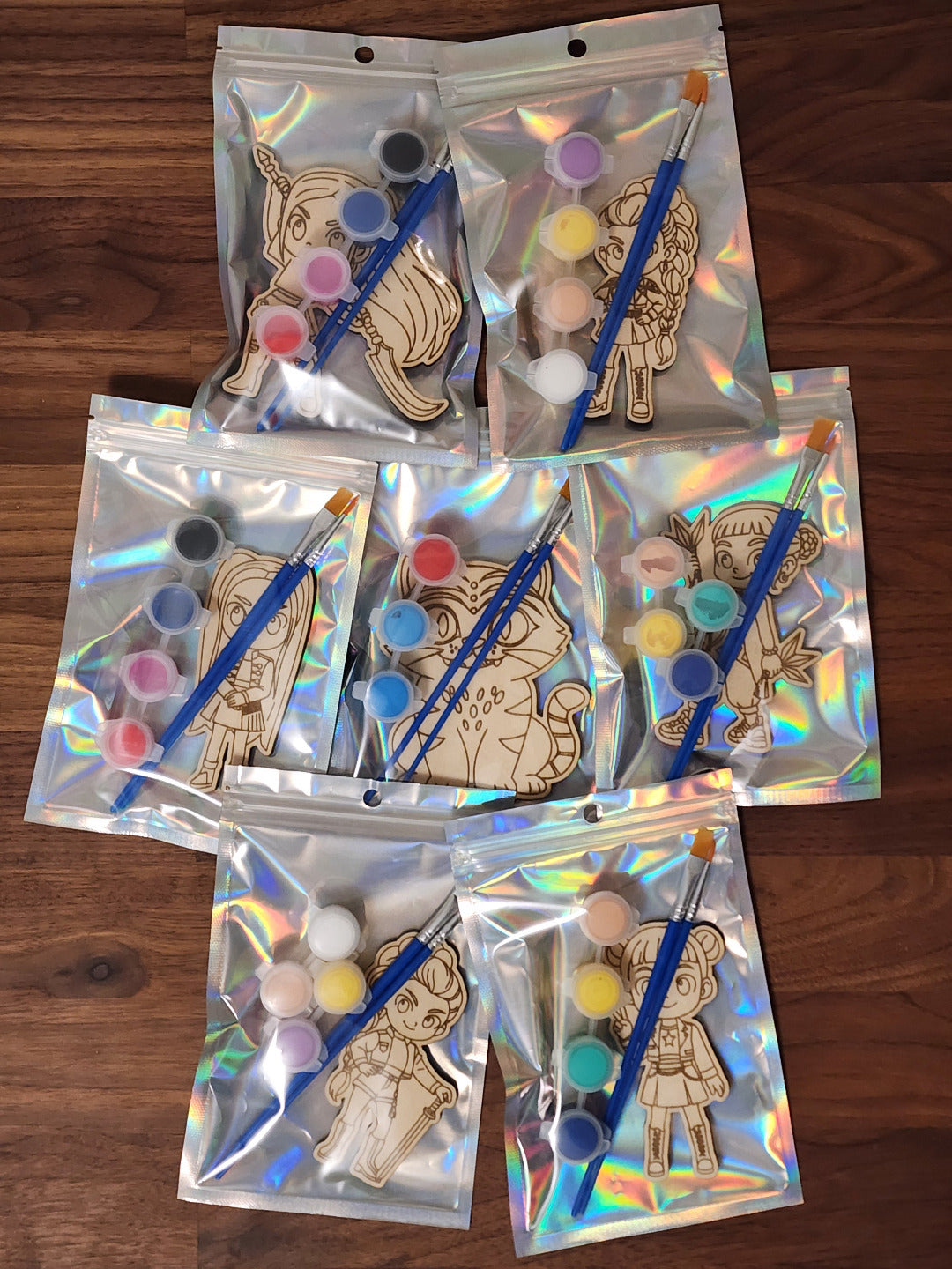 A selection of K-Pop themed wooden engraved paint kits in a holographic bag with paint brushes