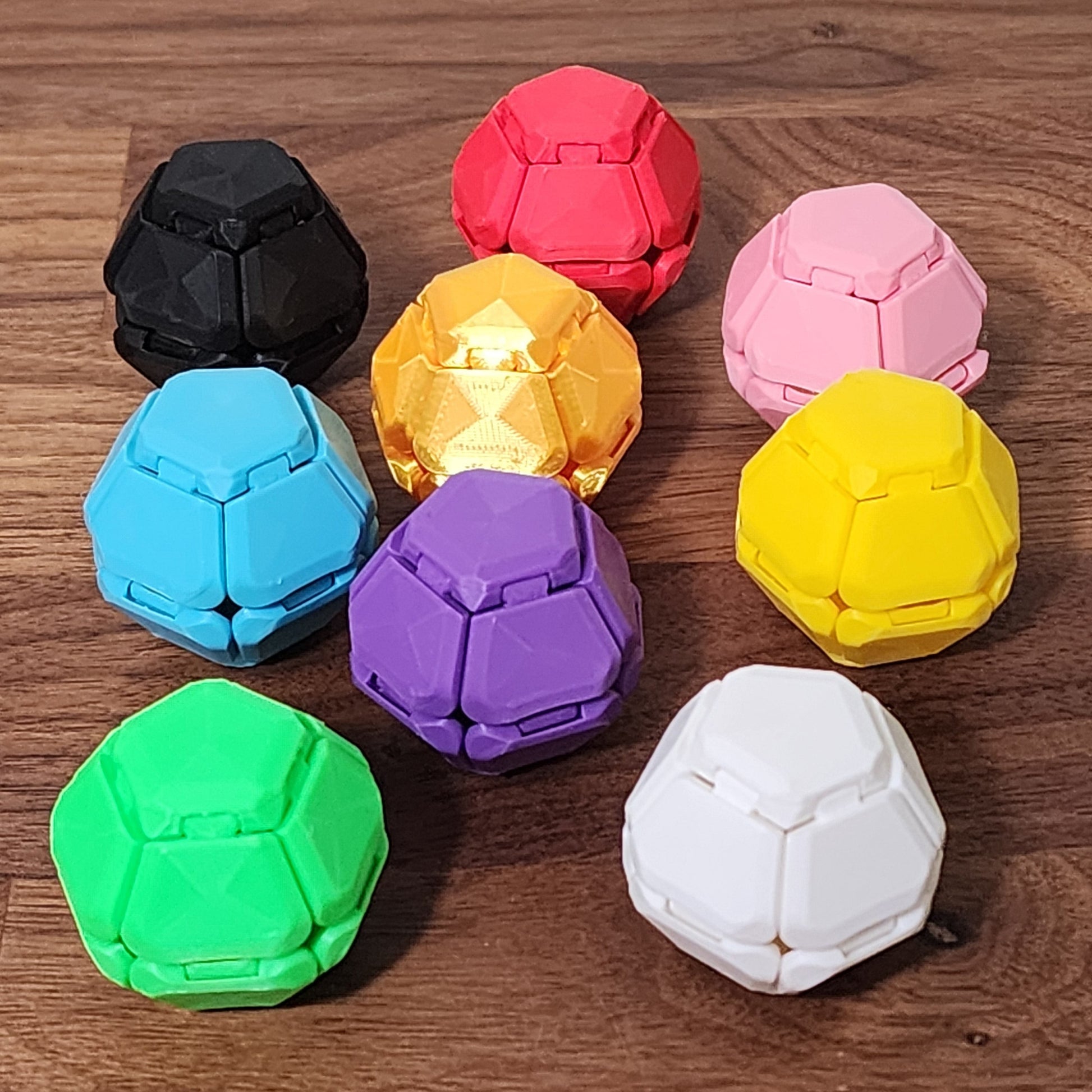 Multiple Penta-Click fidgets in different colors sitting on a wooden desk